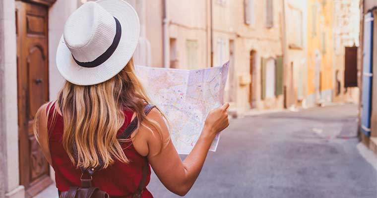 Mujer con mochila y sombrero mirando un mapa en una calle vacía de estilo europeo, representando el uso de consignas de equipaje en Madrid o Barcelona