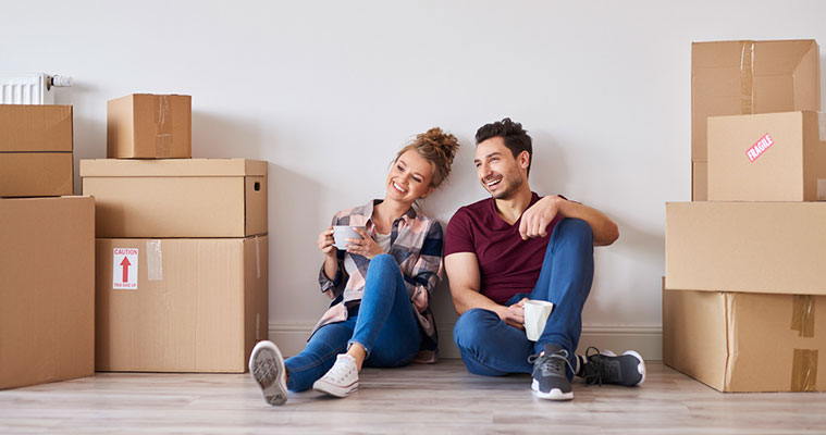 Two people sitting on the floor among moving boxes, enjoying a coffee break while preparing to move