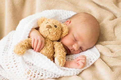Newborn baby sleeping wrapped in a blanket with a teddy bear, symbolising life changes supported by OhMyBox storage.