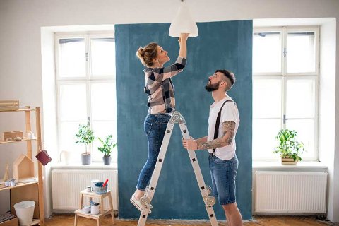 Couple renovating their home together, adjusting a ceiling light with boxes and paint nearby, supported by OhMyBox storage.